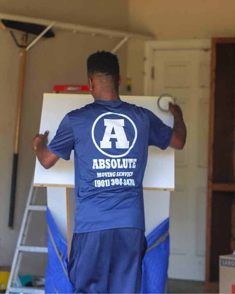 An Absolute crew member in uniform, seen from behind, handling a furniture panel inside a home